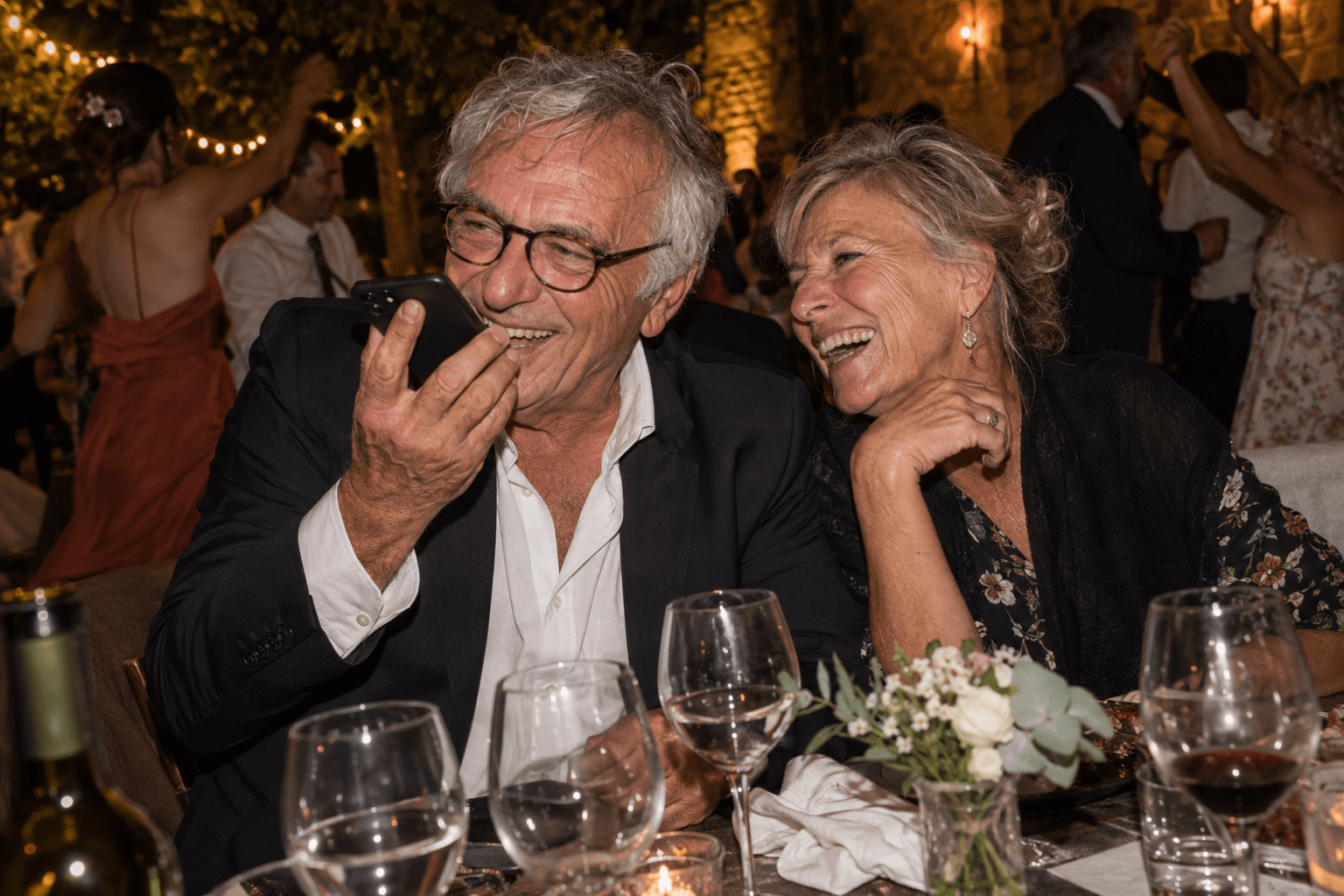 A guest laughs while recording a voice message at a wedding dinner.